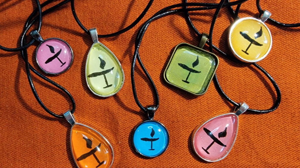 Seven necklace pendants in various colors, each stamped with a chalice of light symbol in black